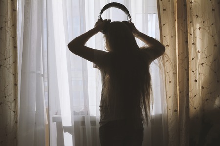 Silhouette of teenager girl wearing headphones in front of the windowの写真素材