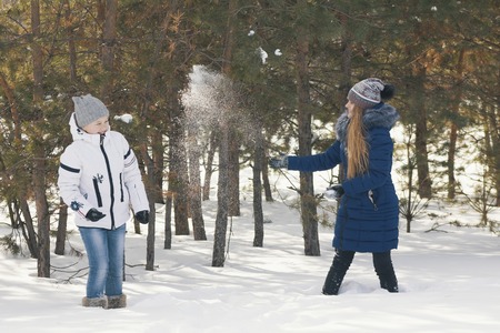 Two teenage girls in warm clothes playing snowballs between the trees in the winterの写真素材