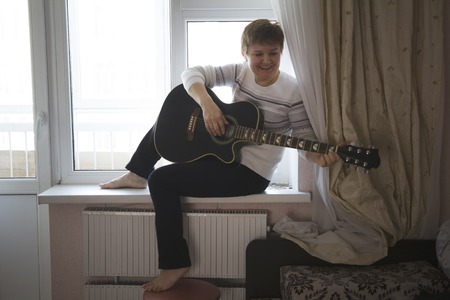Portrait of middle aged woman with guitar near window at home