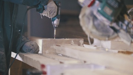 Worker carpenter puts the screws in wooden board at joineryの写真素材