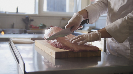 Butcher cutting large piece of fresh raw meat lying on a wooden board in a commercial kitchenの写真素材
