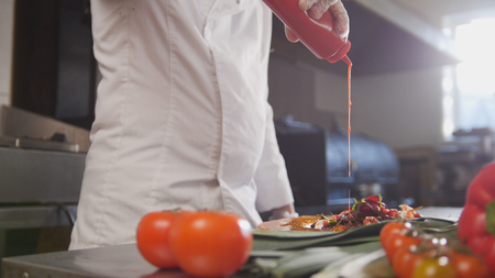 Chef serves the salad adding the sauce, fresh vegetables in the foregroundの写真素材