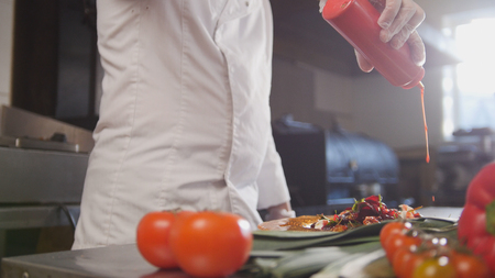 Chef serves the salad adding the sauce, fresh vegetables in the foregroundの写真素材