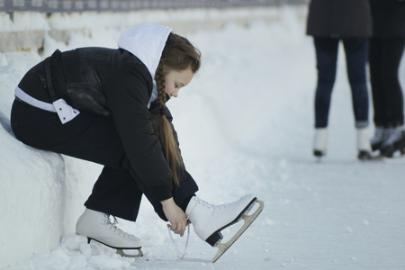 Teenage girl sitting on snow tightening the laces on the skatesの写真素材