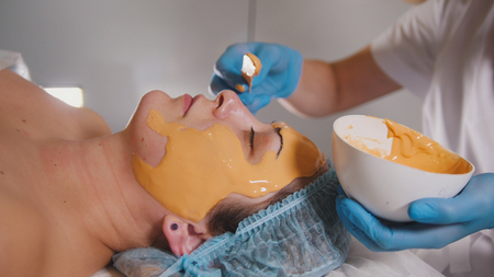 Close up of a person who visiting the beauty salon, fruit mask is applied on the face with a special wooden stickの写真素材