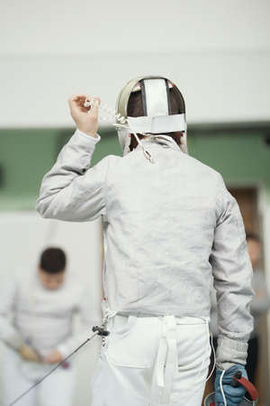 Back of young fencer in white costume and protective maskの写真素材