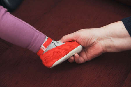 Old woman hand holding feet of toddler girl with shoesの写真素材