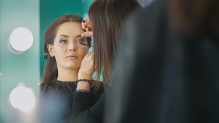 Makeup artist, hairdresser working with young woman in the beauty salon, shaping and coloring eyebrowsの写真素材