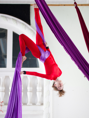 Young attractive air gymnast performs an exercise hanging on aerial silkの写真素材