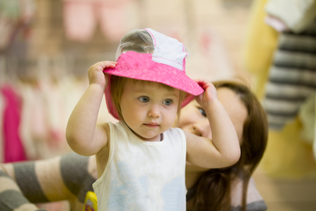 Little caucasian try on the hat during shopping with her momの写真素材