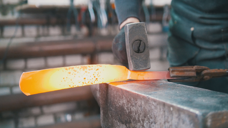 Muscular man blacksmith with hammer in forge creating steel knife