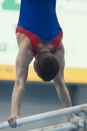 Young man gymnasts competing on the bar at the championshipの写真素材