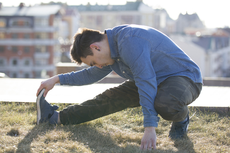 Young male parkour sportsman doing warm-up before acrobatic jumps in front of skylineの写真素材