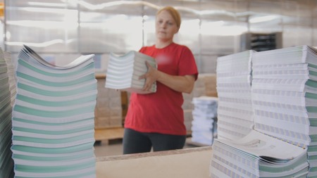 Female worker puts the printed magazines in stacks on the table in the typography