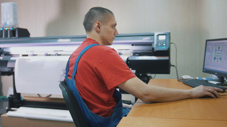 Male worker in typography with computer in front of printing press
