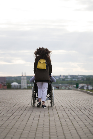 Rear view of young woman walking with disabled man in wheelchair on the quayの写真素材