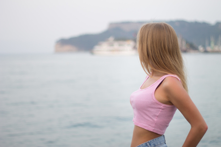 Portrait of unrecognizable young blonde woman looking at mountain by the seaの写真素材