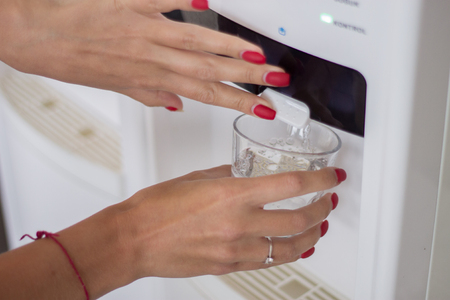 Female hand pours water from a water cooler in glass cupの写真素材