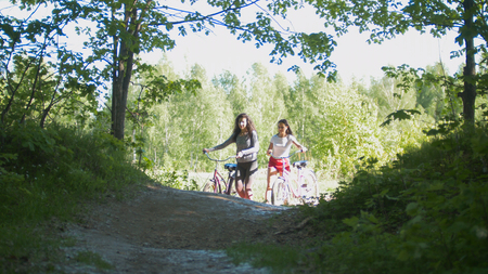 Girlfriend cyclists leave the path of the green thicket, a Sunny dayの写真素材