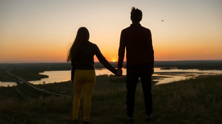 Loving young couple holding hands looking each other at amazing sunset outdoors - close upの写真素材