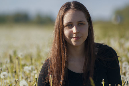 Pretty young woman holding dandelion in summer parkの写真素材