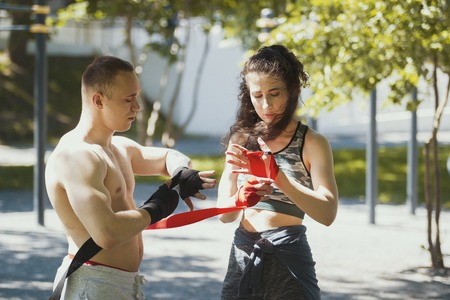 Athletic caucasian man and woman wrapping hands with bandages for workout in summer parkの写真素材