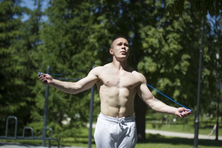 Athletic muscular man jumping with a rope, workout outdoors at sunny dayの写真素材