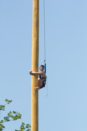 KAZAN, RUSSIA - JUNE 23, 2018: Traditional Tatar festival Sabantuy - A young man climbs on a wooden post at folk tatar festivitiesのeditorial素材