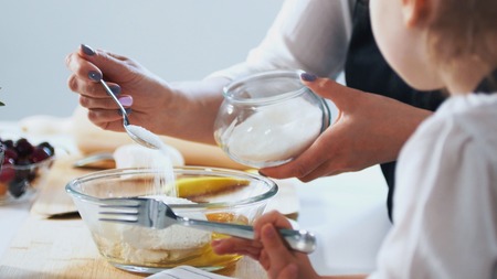 Woman with her child puts sugar in the dough for preparing pancakes