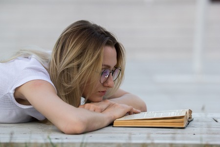 Portrait of young woman reading a book lying on the bench in the parkの写真素材