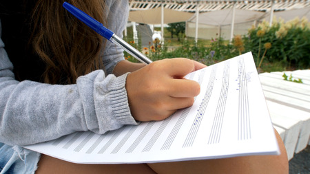 Girl writes music on sheet sitting in park