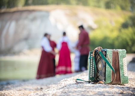 Shot of the accordion, on the background of a group of young people in Russian national red costumesの写真素材