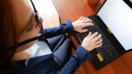 Young red hair officeworker women in glasses is printing on the laptop keyboard. Top-down view