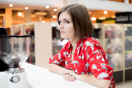 Young girl with a bob haircut and in printed shirt sitting in a coffee shop in a shopping centerの写真素材