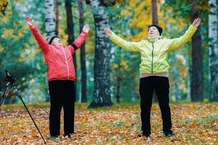 Mature woman doing gymnastics in an autumn park after a scandinavian walkの写真素材