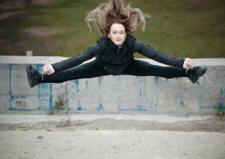 Girl jumping doing splits on the street against the background of a wall with graffiti
