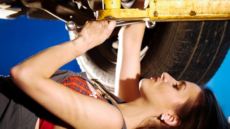 Sexy mechanic girl lying under the car and repairing it. Side angle. Close up shotの写真素材