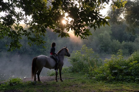 Young woman riding a white horse on a beautiful landscape. Clear lake at morning fog. Sunriseの写真素材