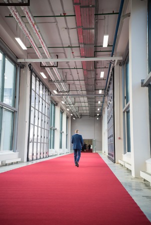 Middle aged man walking on a red carpet towards a conference hallの写真素材