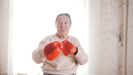 An old senior women boxing in red gloves, looking aggressively funnyの写真素材