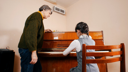 A little girl playing piano on music lesson. A teacher near by herの写真素材