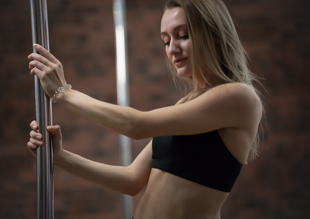 Young attractive woman in sport bra staying holding a pole