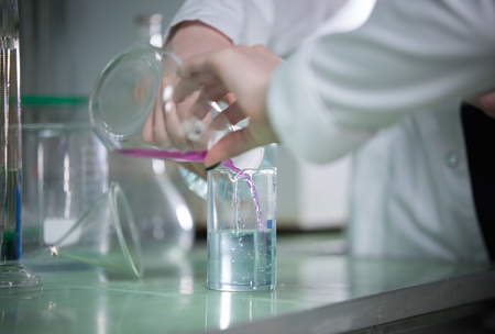 Table full of flasks. Chemical lab. Hands pouring liquidの写真素材