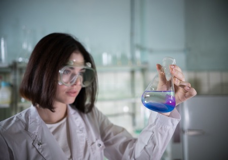 Chemical laboratory. Young woman holding a flask with blue and purple exfoliating liquid in it. Portraitの写真素材