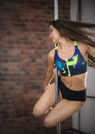 Girl in sport clothes training pole dance in a studio