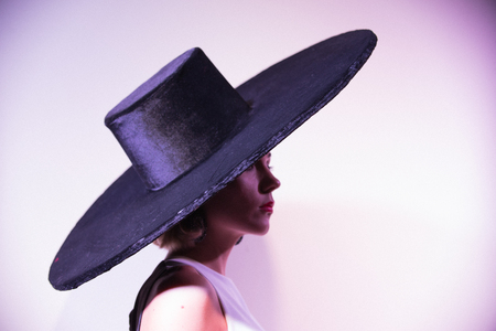 Young attractive woman standing on the background of a white wall in big hat