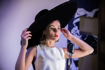 Young attractive woman standing on the background of a white wall in big hat, singing. Bright yellow eyesの写真素材