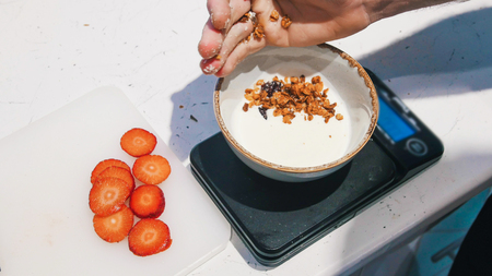 Serving the breakfast. White yogurt in the bowl. Sprinkling granola on white yogurtの写真素材