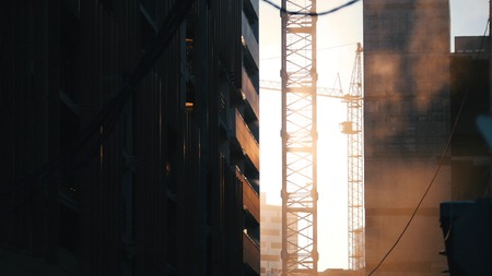 Construction site. Working tower crane. Dust soaring in the air. Hanging wires on the foreground. Sunsetの写真素材