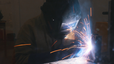 A welder in helmet doing his job. Welding process. Smoke and sparks